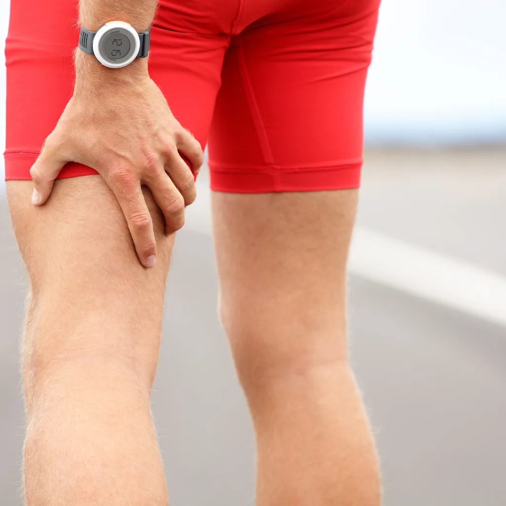 Runner in red kit stopped on the road, gripping the back of a strained hamstring